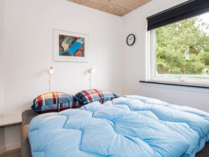 A bedroom with a bed, a clock, a window with a view of trees, and a framed artwork on the wall.