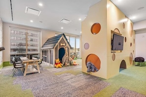 Un espace de jeux pour enfants comprenant une bibliothèque, une maison de jeu et un téléviseur fixé au mur.