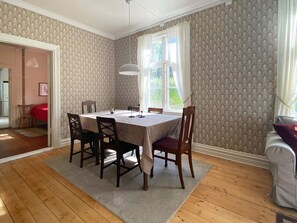Une salle à manger avec une table dressée pour quatre personnes, entourée de chaises, d’un lustre et d’une fenêtre ornée de rideaux.
