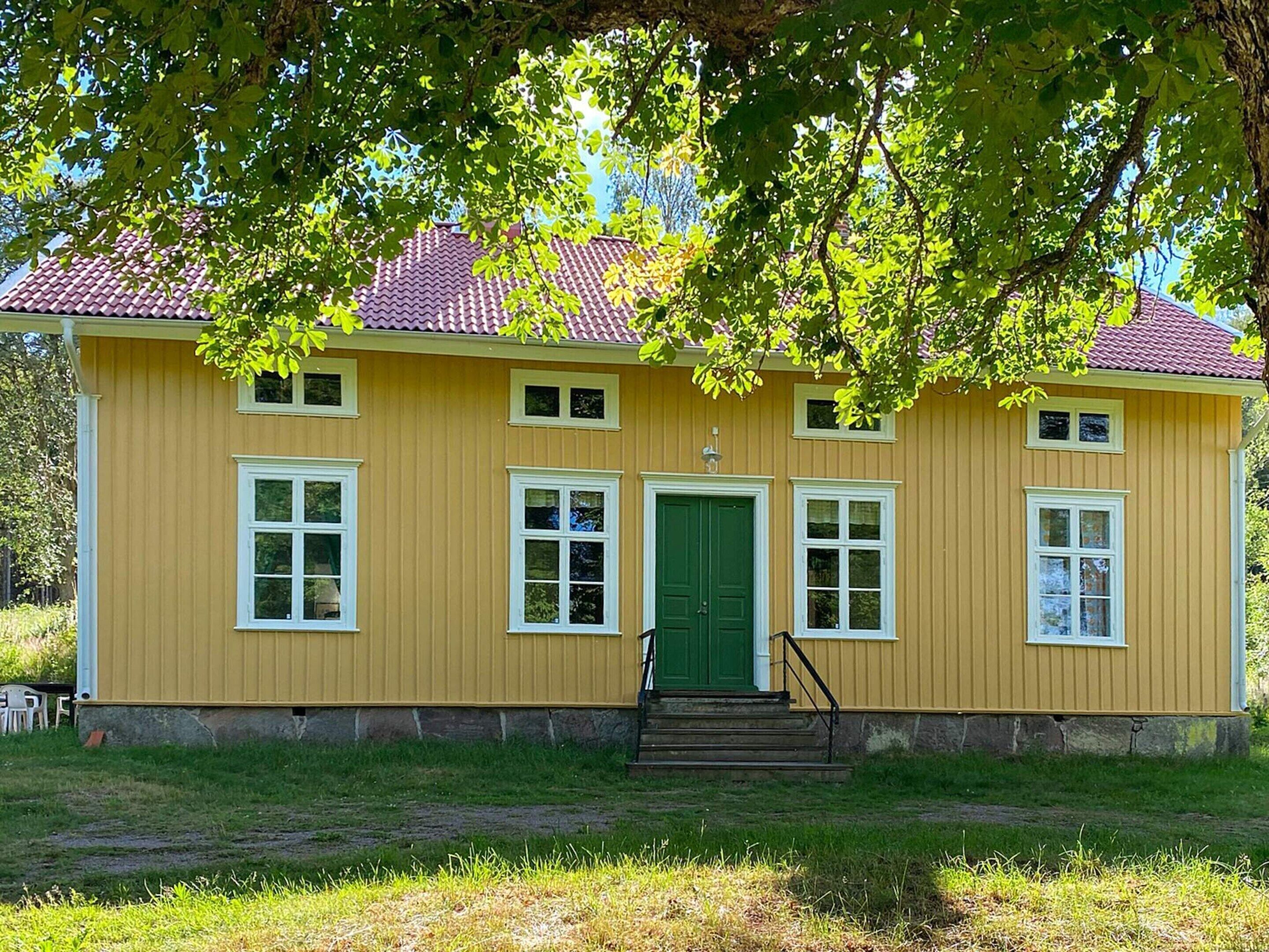 A yellow building with a green door and windows, surrounded by grass and trees.