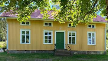 A yellow building with a green door and windows, surrounded by grass and trees.