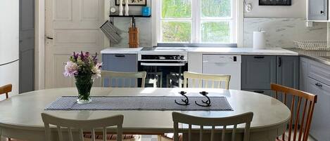 Una cucina con tavolo da pranzo, sedie, fornello e una finestra vista su del verde.