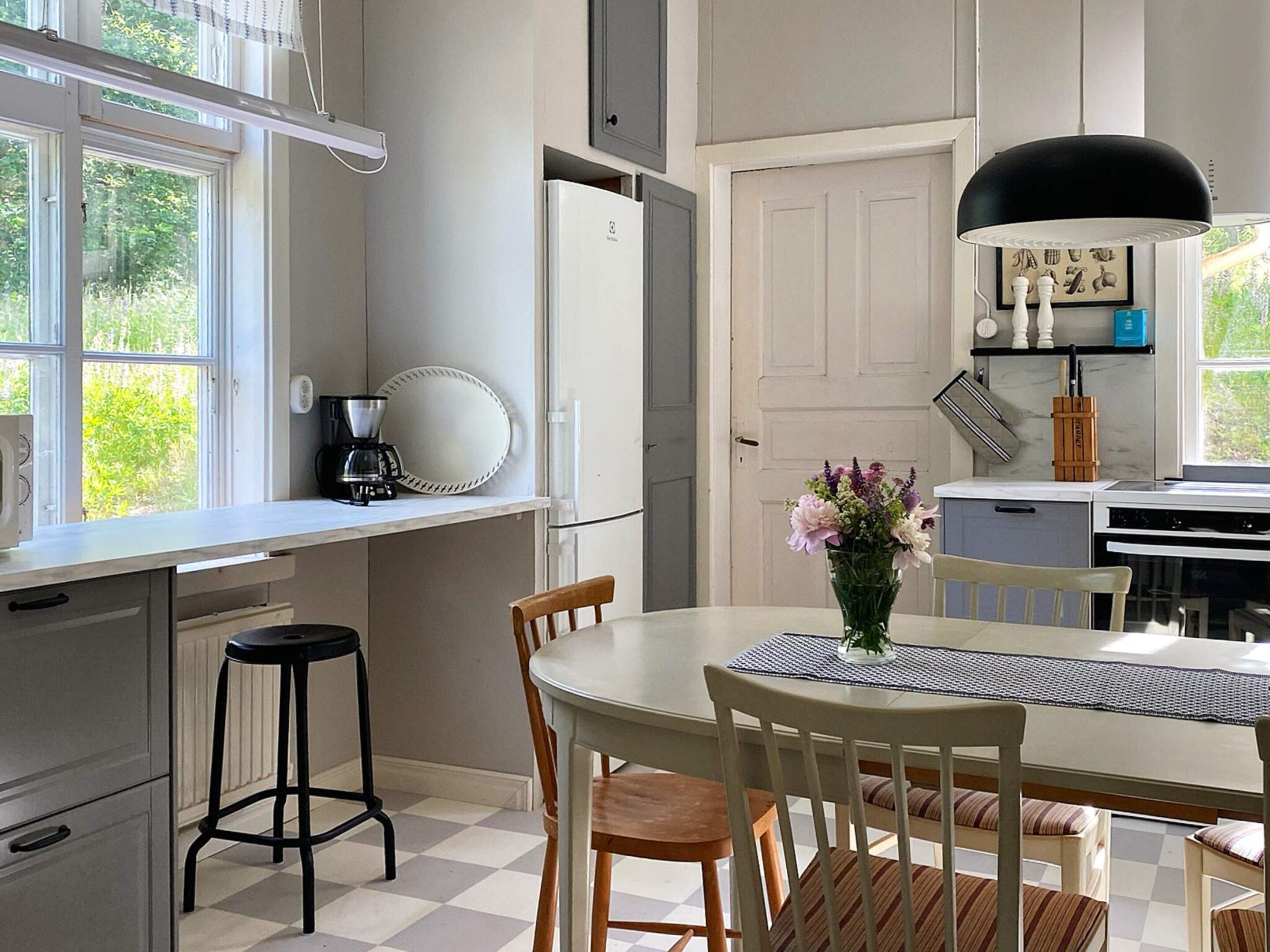 A kitchen with a dining table, chairs, a coffee maker, and a refrigerator.