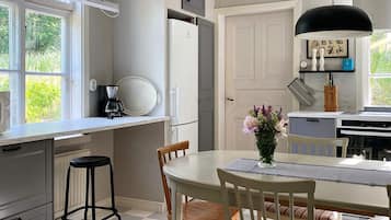 A kitchen with a dining table, chairs, a coffee maker, and a refrigerator.
