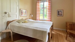 Une chambre avec deux lits, un plancher en bois, une fenêtre avec des rideaux, une porte et un petit tapis rond.