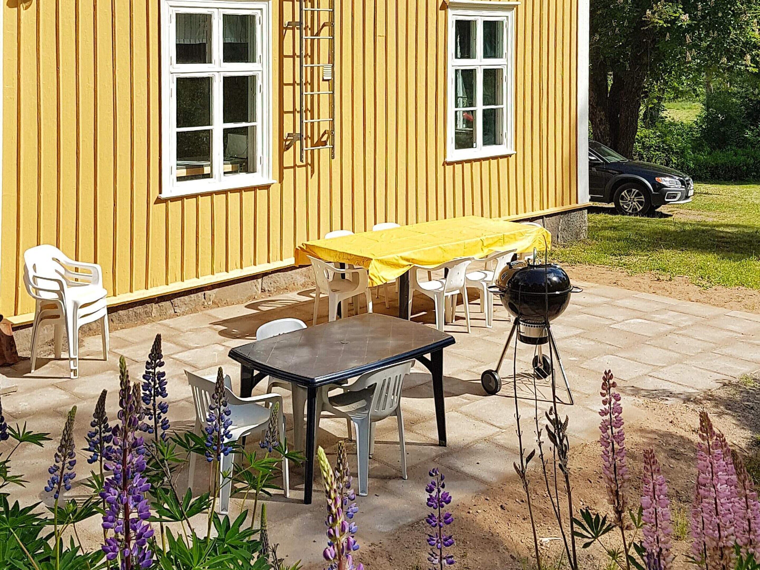 A yellow building with a patio area featuring a table and chairs, a barbecue grill, and a ladder leaning against the wall.