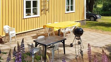 A yellow building with a patio area featuring a table and chairs, a barbecue grill, and a ladder leaning against the wall.