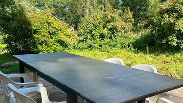 An outdoor dining area with a dark wooden table and white plastic chairs.
