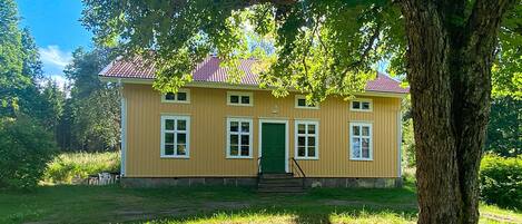 A two-story house with a red-tiled roof, a green door, and a staircase leading to the entrance.