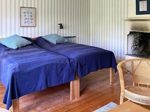 A room with two beds, a wicker chair, a fireplace, and a framed picture on the wall. - 4 Star Holiday Home in Sandhem (Sandhem)