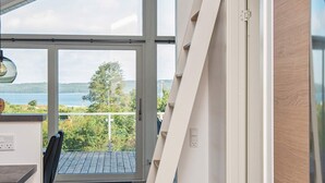 Un intérieur moderne avec vue sur un lac, une terrasse en bois et un coin repas comprenant une table et des chaises.