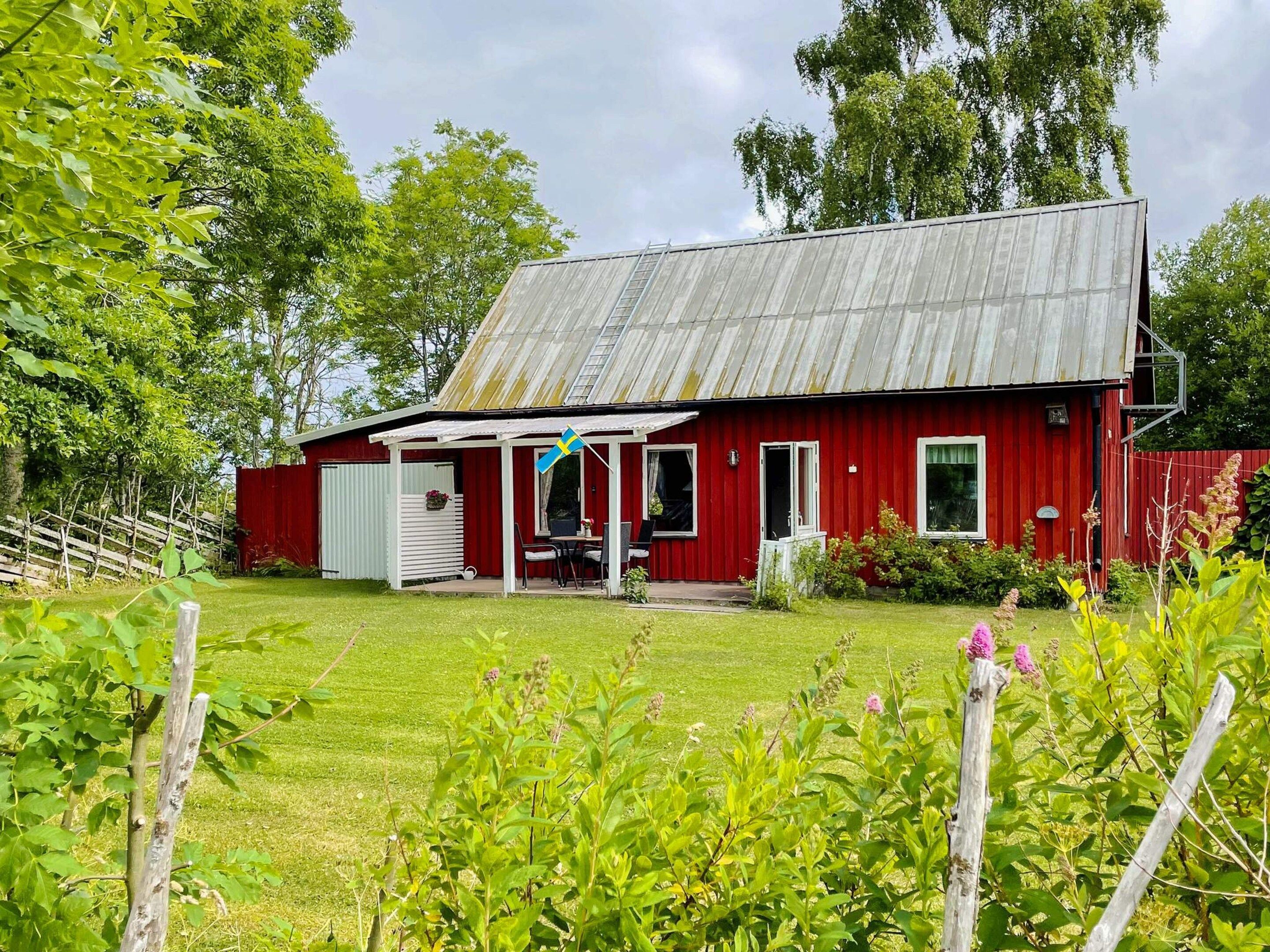 A red barn with a porch and a flag, surrounded by greenery and trees.
