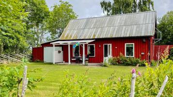 A red barn with a porch and a flag, surrounded by greenery and trees.