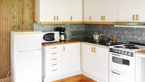 A compact kitchen with white cabinets, a microwave, a coffee maker, a stove, and a refrigerator. - 4 Person Holiday Home in Hogklint (Visby)