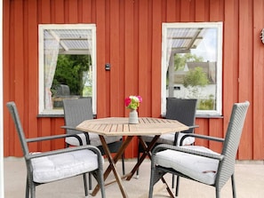 A red wooden building with a small patio area featuring a round table and four wicker chairs. - 4 Person Holiday Home in Hogklint (Visby)