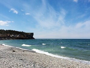 A pebble beach with waves, a cliff, and houses in the background. - 4 Person Holiday Home in Hogklint (Visby)