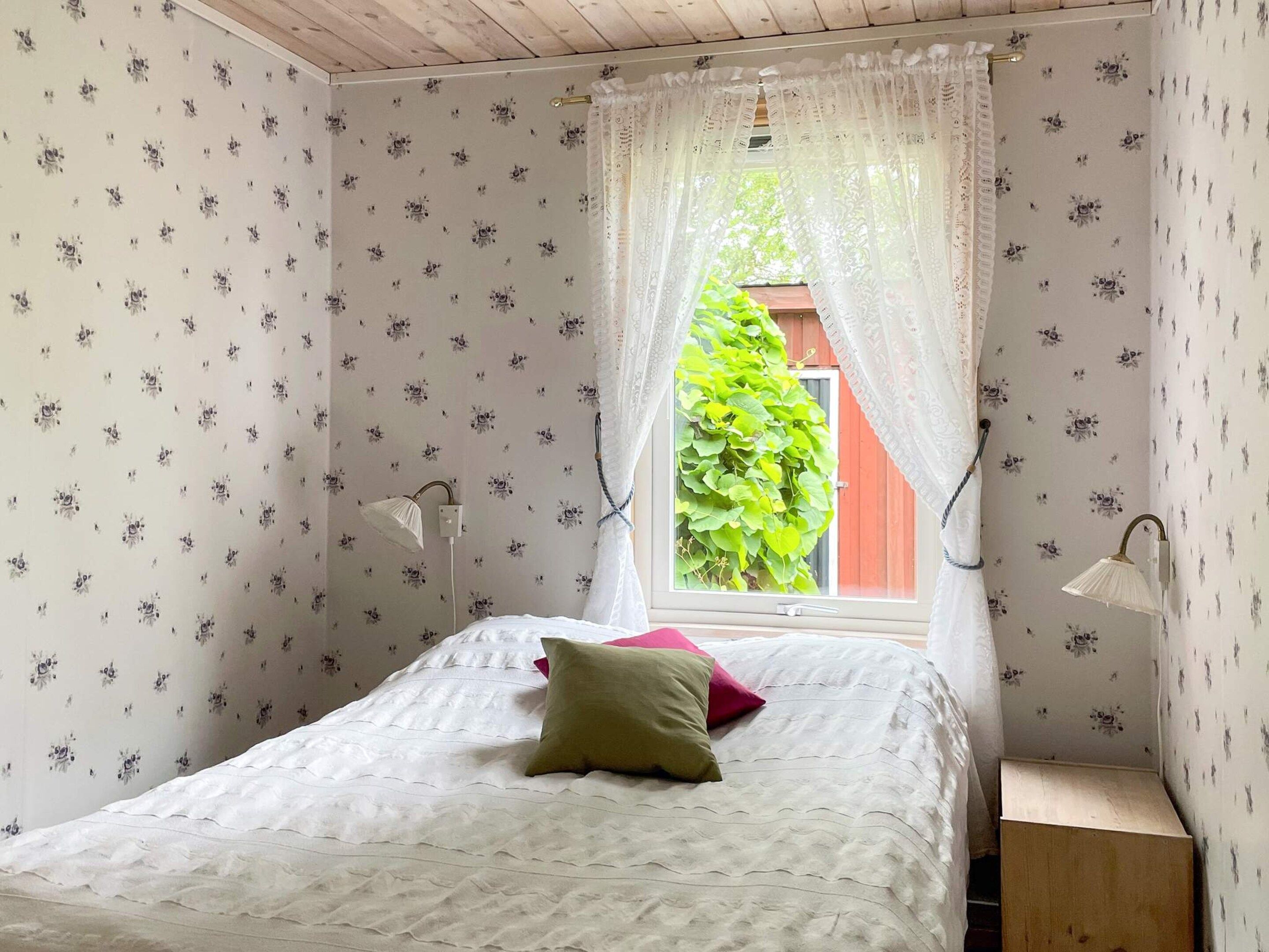 A bedroom with a single bed, a window with a view of greenery, and patterned wallpaper.