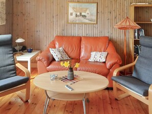 A cozy living room with a leather sofa, two armchairs, a wooden coffee table, and a bookshelf.