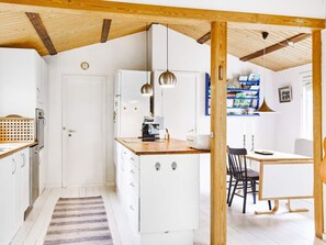 Eine kleine Küche mit weißen Schränken, einer Holz Arbeitsplatte und hängenden Pendelleuchten.