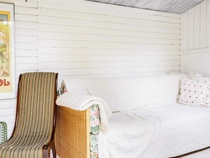 Une pièce avec un canapé blanc, un fauteuil en osier et un tableau encadré accroché au mur.