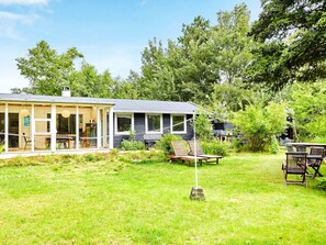 Una casa moderna con un amplio porche de cristal, un comedor y un jardín con mobiliario exterior.