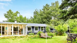 Una casa moderna con un amplio porche de vidrio, un comedor y un jardín con mobiliario exterior.