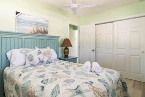 Ein Schlafzimmer mit einem Bett, einem Deckenventilator, einem Nachttisch mit Lampe und einer Tür.