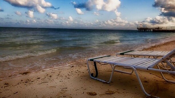 Une plage avec une chaise longue en métal et une jetée en arrière-plan.