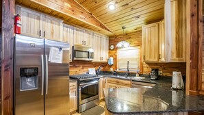 A kitchen with wooden cabinets, stainless steel appliances, a microwave, and a coffee maker. - Papa Bear Log Cabin at the Buffalo River (Compton)