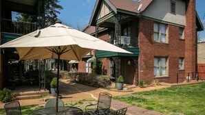 Un espace patio avec une table et des chaises, un grand parasol et un bâtiment en briques en arrière-plan.