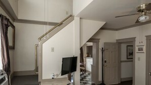 Un vaste espace de vie comprenant un escalier, un ventilateur de plafond, un téléviseur à écran plat et une table à manger agrémentée d’un chemin de table à motifs floraux.