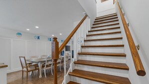 A wooden staircase with white walls and a dining area with a table and chairs. - Pet-Friendly Beach Blessing Steps from the Gulf (Miramar Beach)