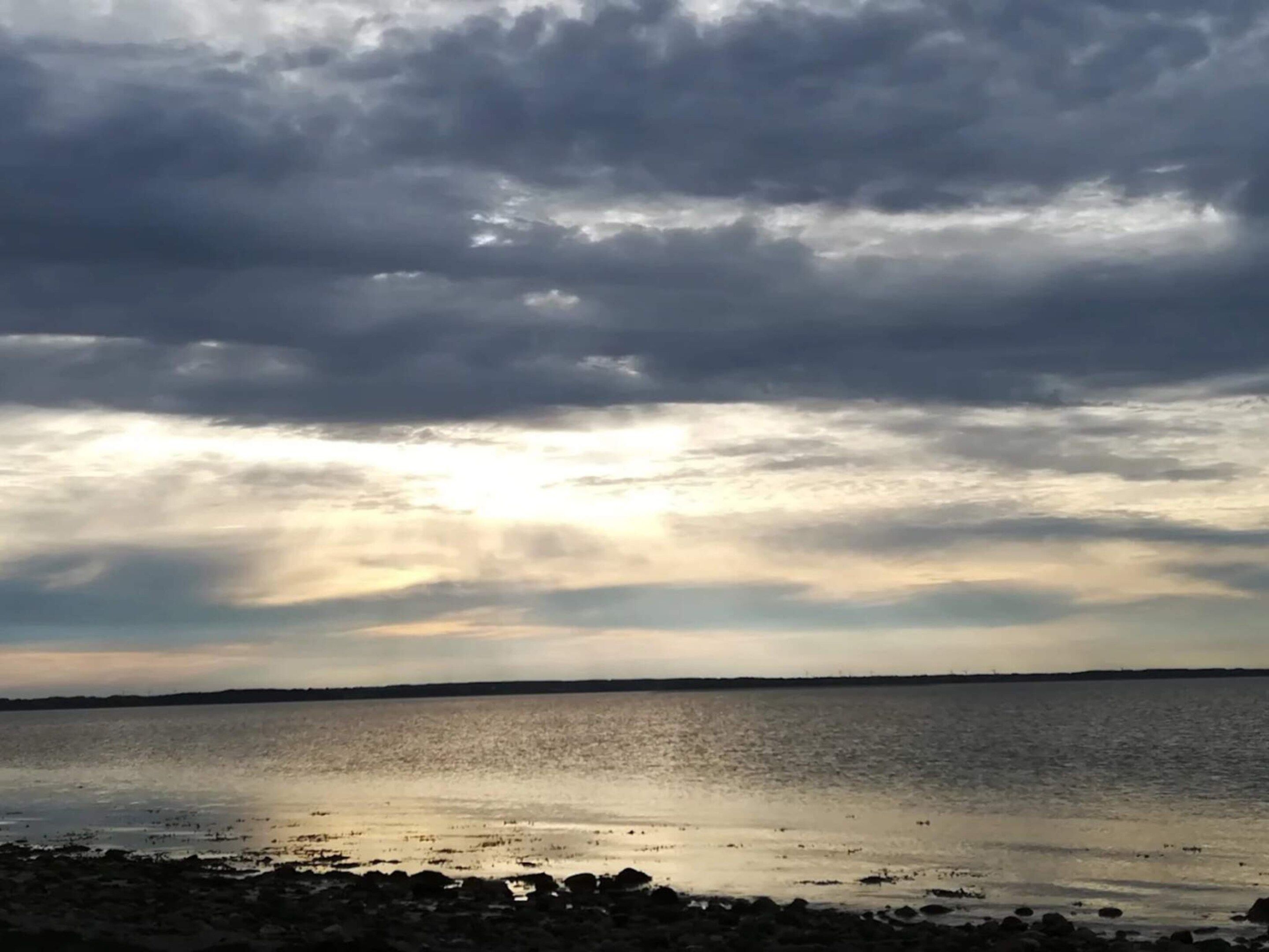 Un paysage côtier avec une mer calme, une côte rocheuse et un ciel nuageux.