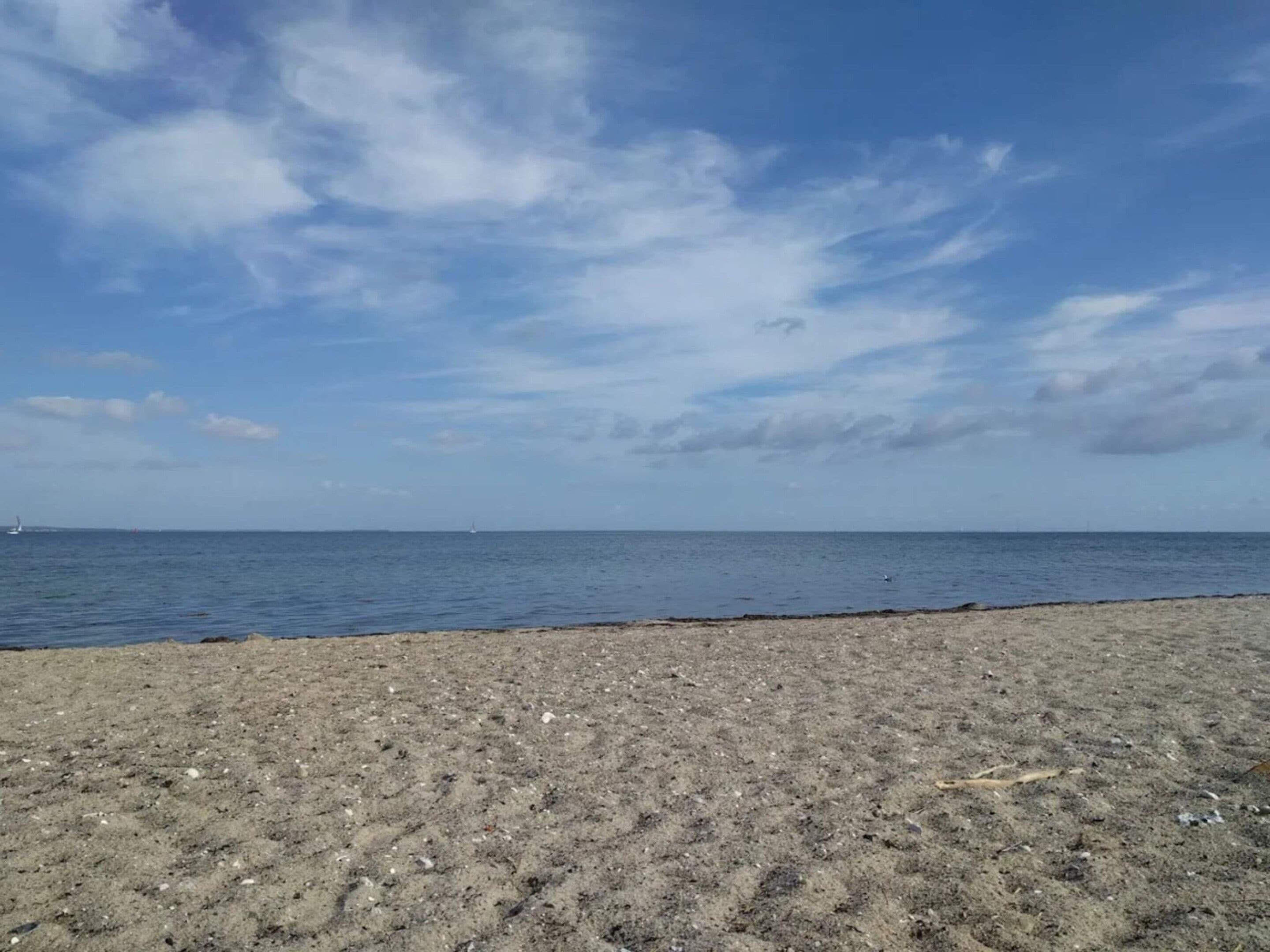 A beach with a sandy shore and a calm sea under a partly cloudy sky.