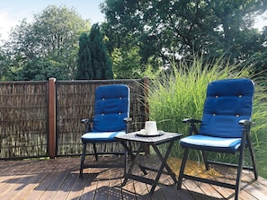 A deck with two blue chairs and a small table, surrounded by a bamboo fence and tall grass. - 5 Person Holiday Home in Tranekaer (Tranekaer)