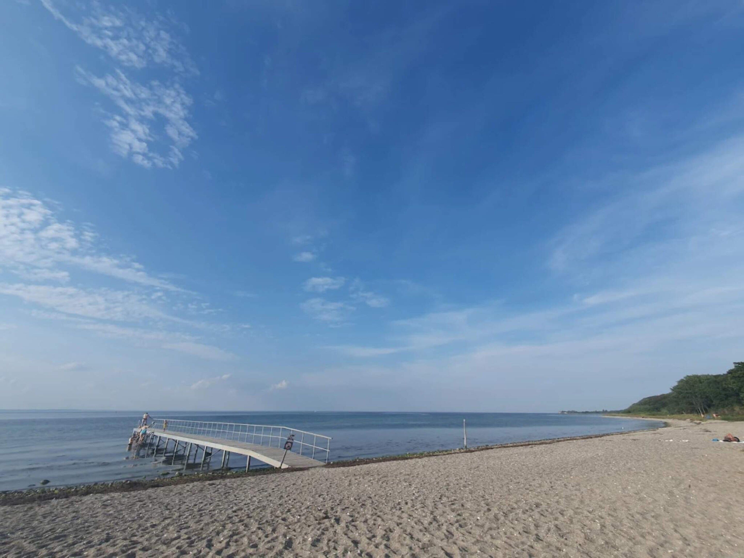 A beach with a pier extending into the water, a clear sky, and a calm sea.