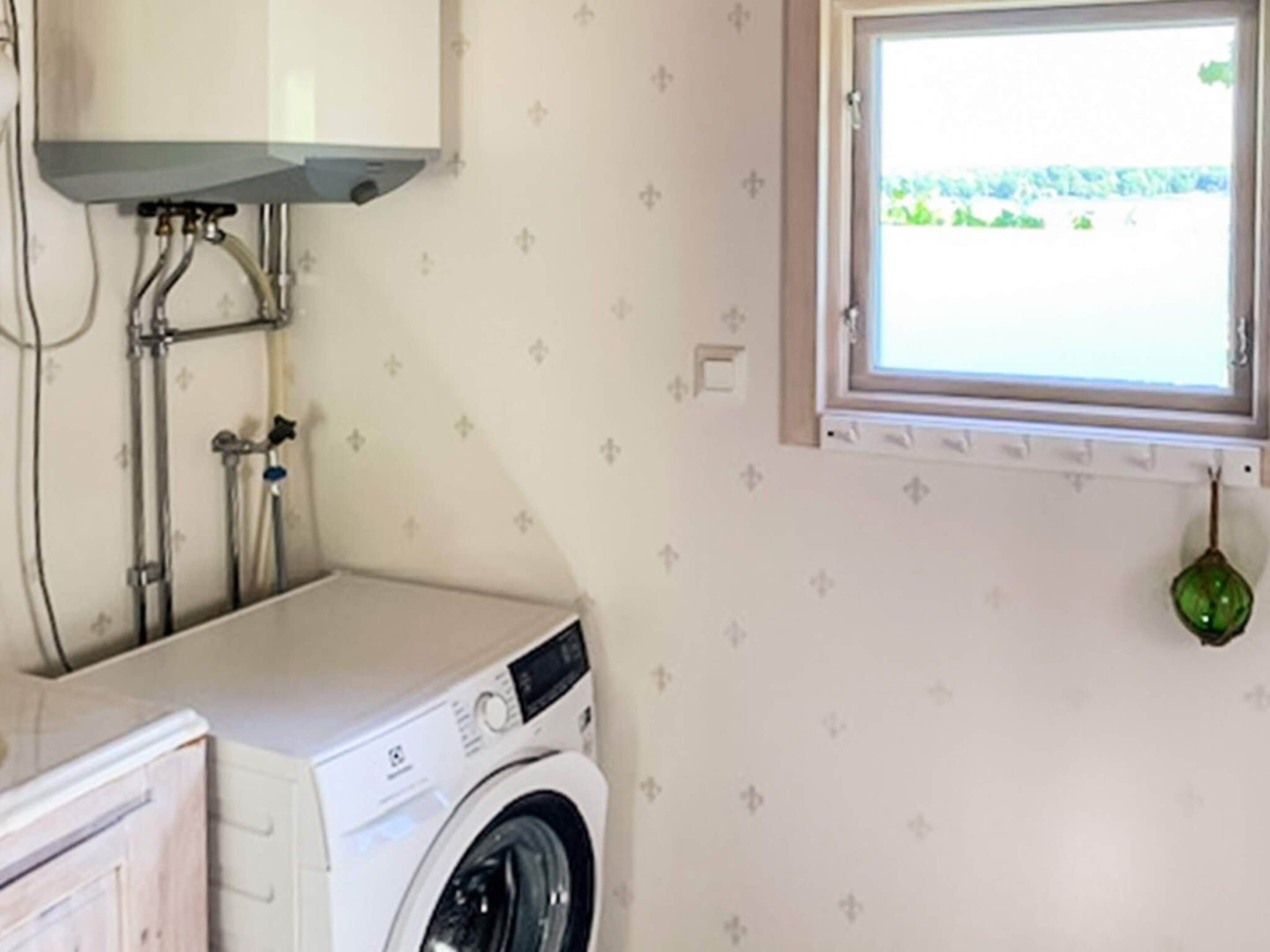 A laundry room with a washing machine, a window, and a green hanging ornament.