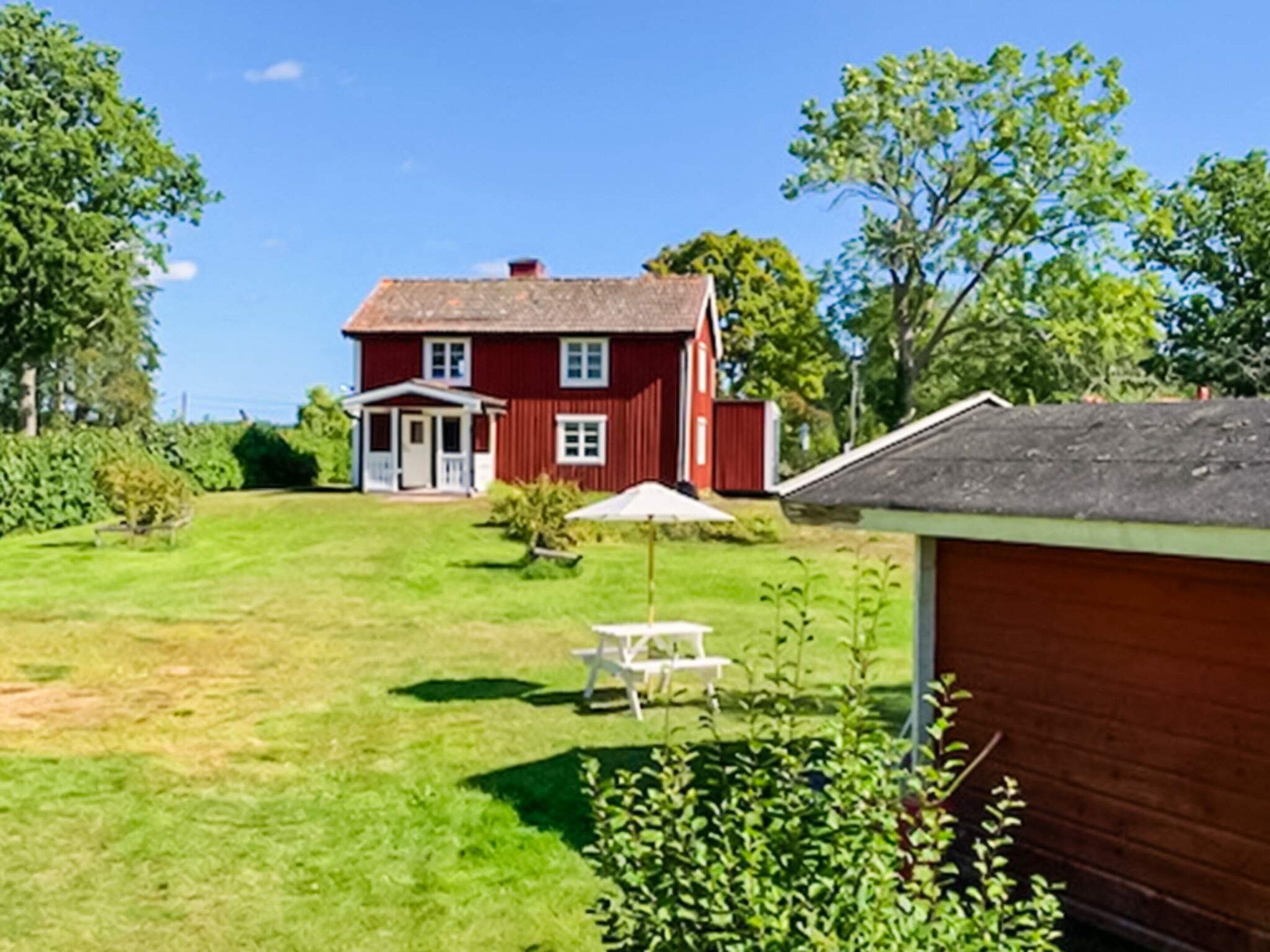 A red house with a front porch, a small garden, and a table with chairs.