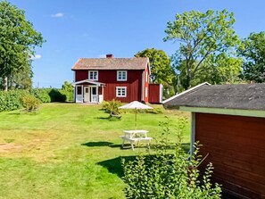 A red house with a front porch, a small garden, and a table with chairs. - 5 Person Holiday Home in Loftahammar (Loftahammar)