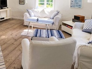 A modern living room with a white sofa, a small white table, and a television on a stand.