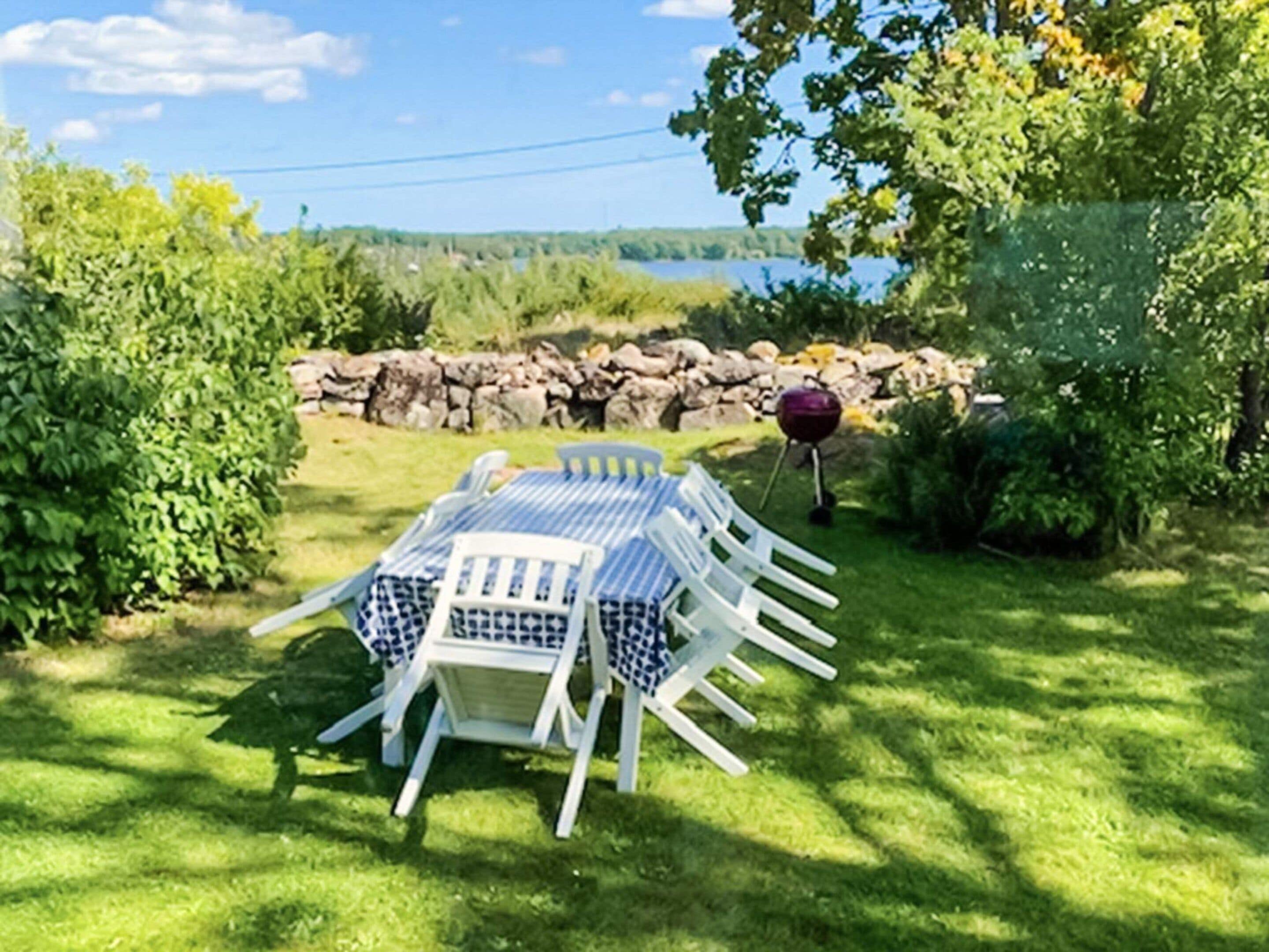 A table and chairs set outdoors with a view of a lake and trees.
