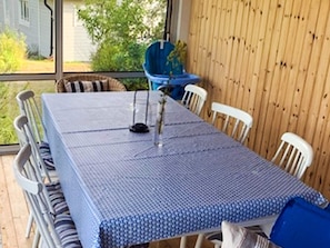 A dining area with a table covered by a blue tablecloth, surrounded by white chairs. - 5 Person Holiday Home in Loftahammar (Loftahammar)