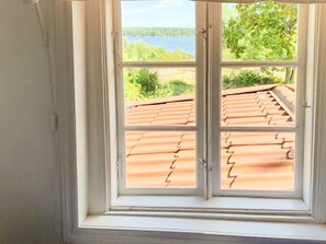 A window with a view of a red-tiled roof and greenery outside.