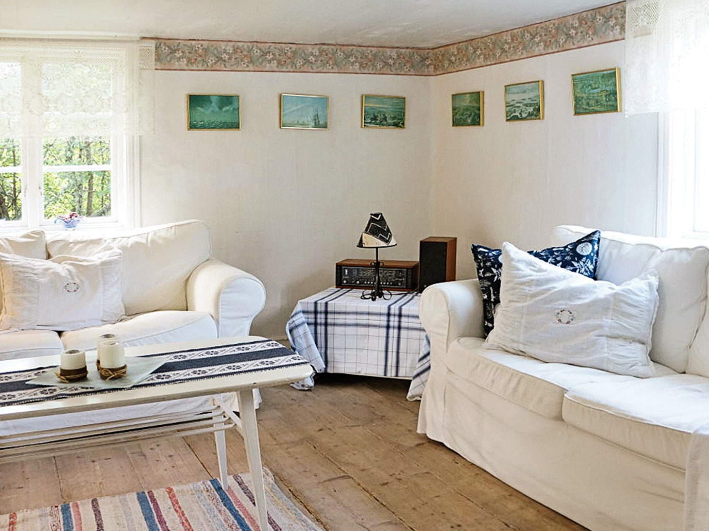A room with two white sofas, a small table with a lamp, and a wall with six framed pictures.