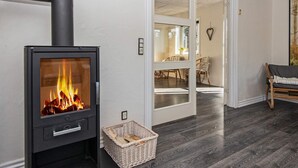 A modern living room with a wood-burning stove, dark wooden flooring, a wicker basket, and a dining area with wicker chairs.