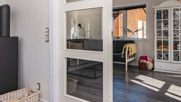 A room with a black refrigerator, a wicker basket, a white cabinet with glass doors, and a window with a view of a brick building.