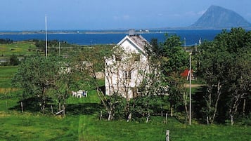 A white house with a sloped roof surrounded by greenery, a clear sky, and a distant mountain.