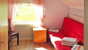Ein gemütliches Zimmer mit Holzboden, einem roten Sofa, einem kleinen Holztisch und einem Fenster mit Vorhängen.