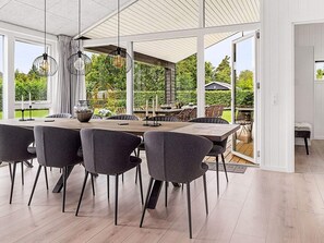 A modern dining area with a large table and chairs, large windows, and a view of the garden.