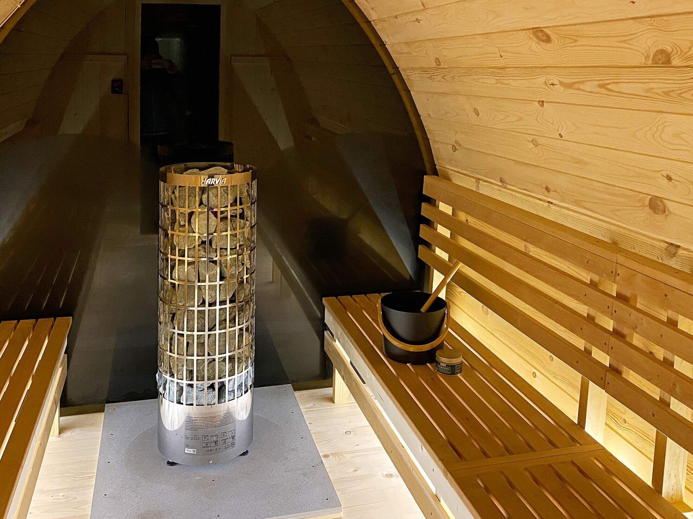 Uma sauna com aquecedor de pedra, bancos de madeira e parede de madeira.